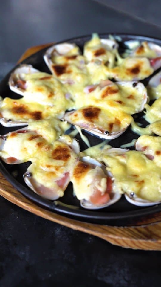 Machas gratinadas servidas en una fuente negra